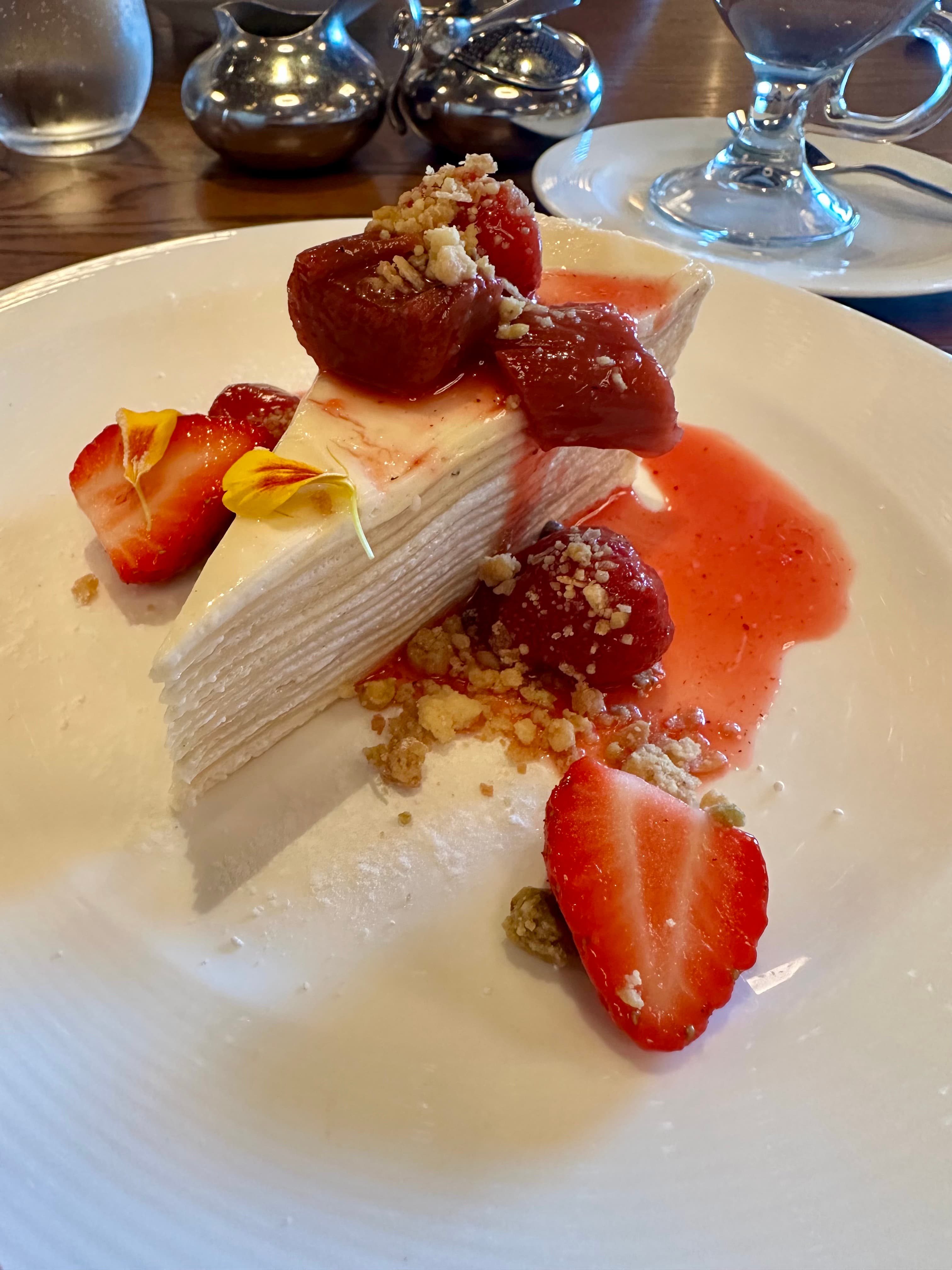 Erdbeer-Crêpe-Torte mit Erdbeersauce und Blüten auf weißem Teller