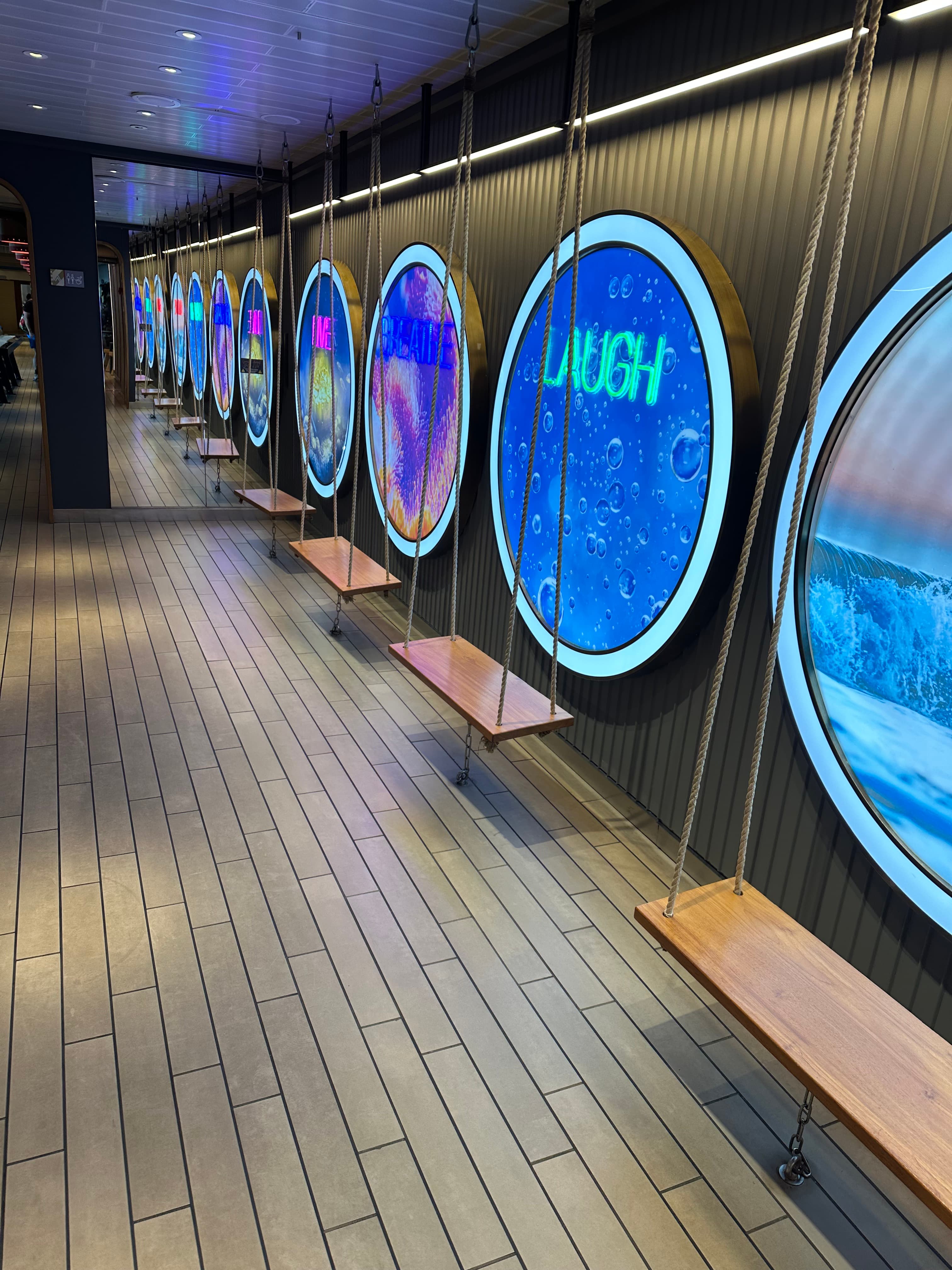 LED-Oval-Screens an der Wand mit Schaukeln davor — LAUGH in Neon auf Meeresblau